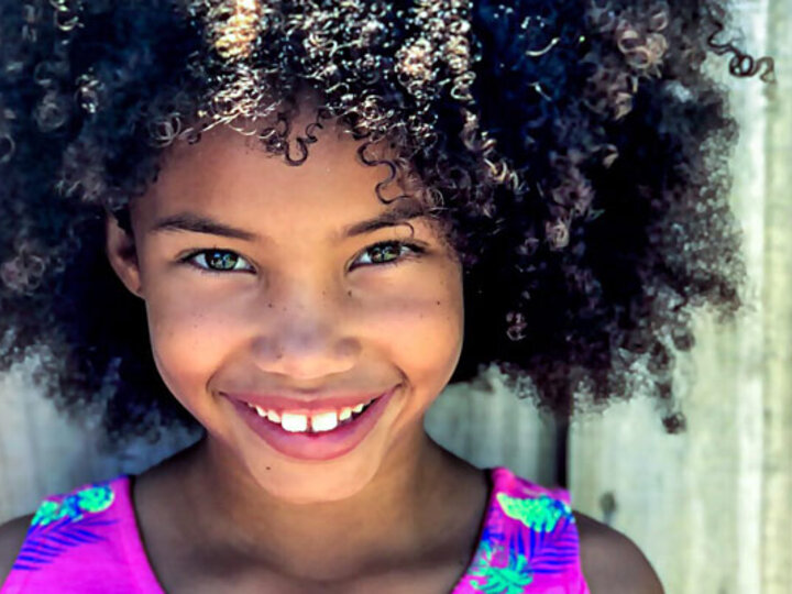  Young African-American girl with curly hair smiling.